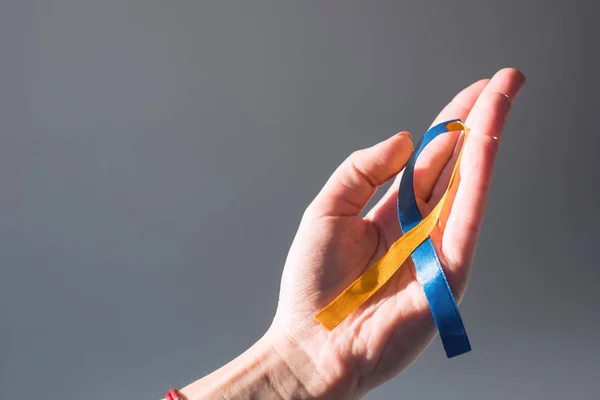 Female hand holding Down Syndrome Day symbol blue and yellow ribbon isolated on grey — Stock Photo