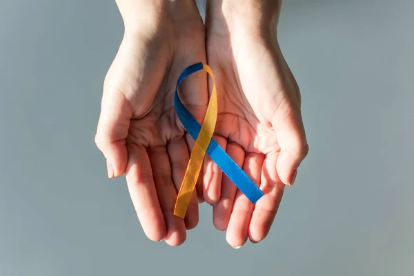 Female hands holding Down Syndrome Day symbol blue and yellow ribbon isolated on grey — Stock Photo