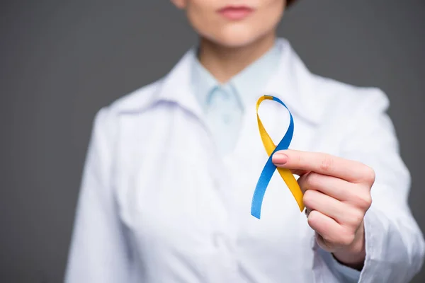 Médecin femme tenant un ruban bleu et jaune pour la Journée du syndrome de Down isolé sur gris — Photo de stock