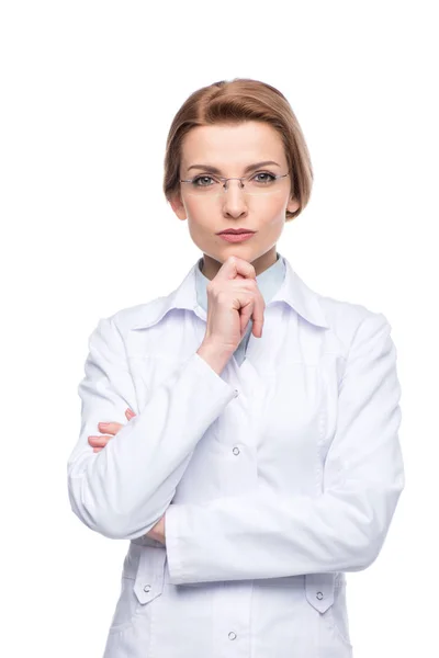 Jeune femme médecin souriante portant des lunettes avec la main sur le menton isolé sur blanc — Photo de stock