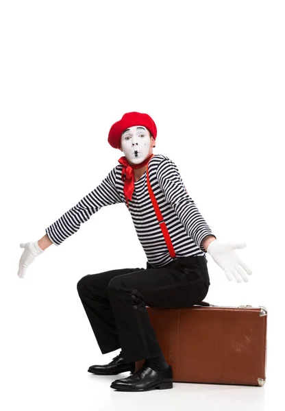 Mime assis sur une valise brune et montrant un geste d'haussement d'épaules isolé sur blanc — Photo de stock