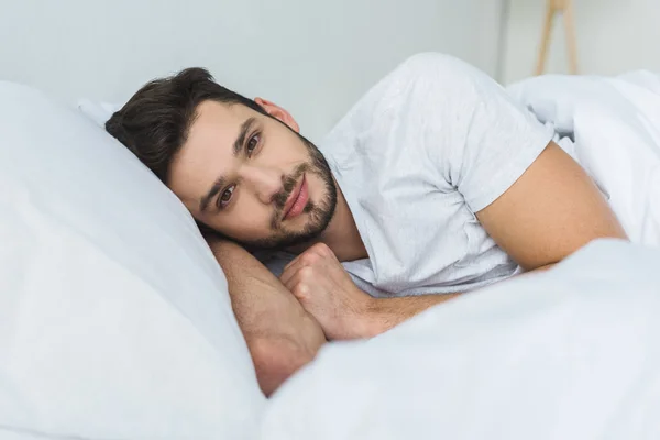 Homem bonito deitado na cama e olhando para a câmera de manhã — Fotografia de Stock