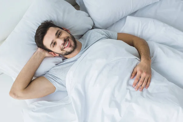 Blick von oben auf einen fröhlichen Mann, der morgens im Bett liegt — Stockfoto