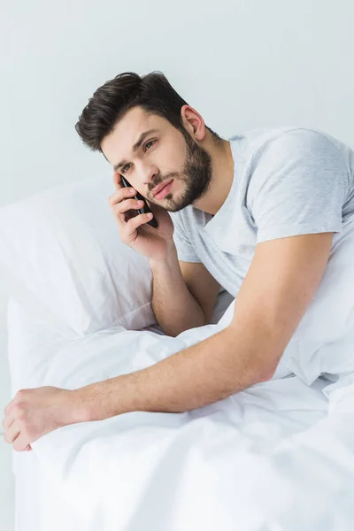Бородатий чоловік лежить на ліжку і розмовляє на смартфоні — стокове фото