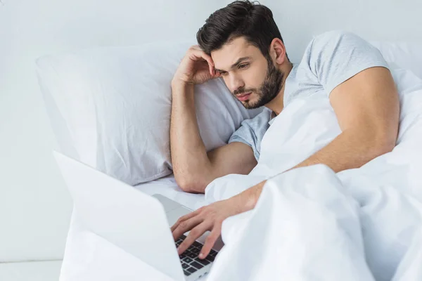 Homme barbu se détendre sur le lit et en utilisant un ordinateur portable — Photo de stock
