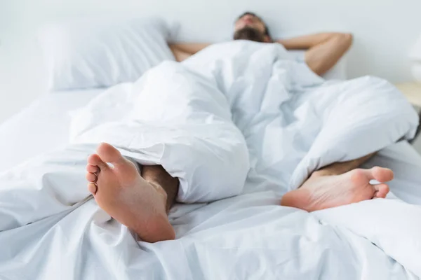 Selective focus of man sleeping on bed, feet on foreground — Stock Photo