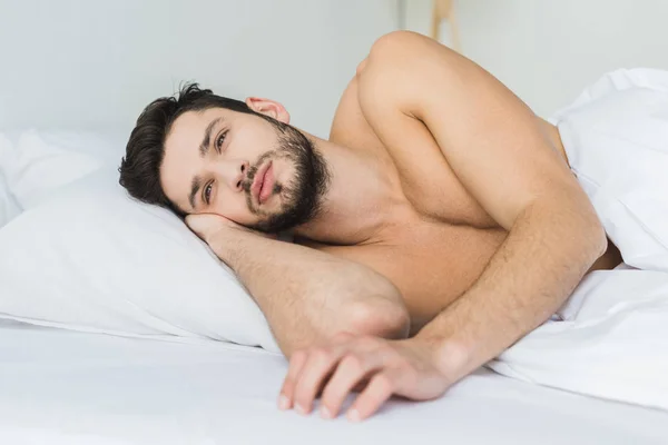Handsome shirtless man lying on white bed in the morning — Stock Photo