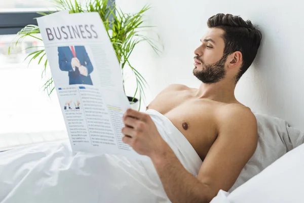 Hemdloser bärtiger Mann, der morgens im Bett Wirtschaftszeitung liest — Stockfoto