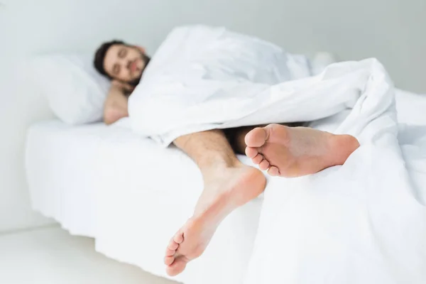 Selektiver Fokus des schlafenden Mannes auf dem Bett, Füße im Vordergrund — Stockfoto