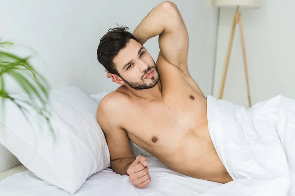 Bonito sem camisa homem relaxante no branco cama — Fotografia de Stock