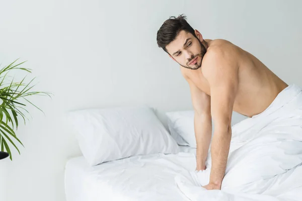 Schöner Mann ohne Hemd posiert morgens auf weißem Bett — Stockfoto