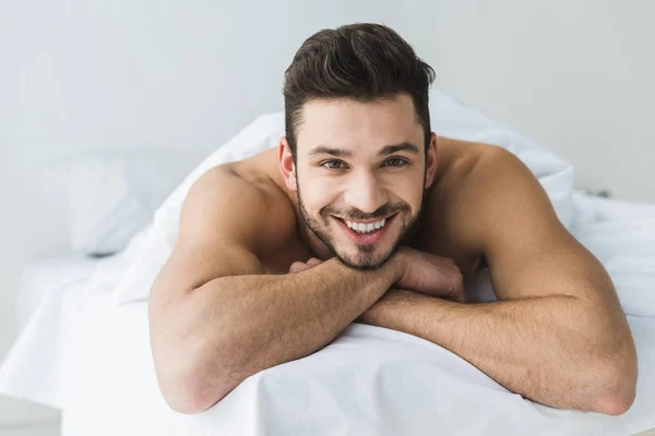 Beau homme joyeux s allongé sur lit blanc et regardant la caméra — Photo de stock