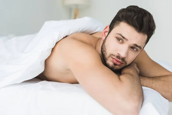 Красивый бородатый мужчина лежит на белой кровати — стоковое фото