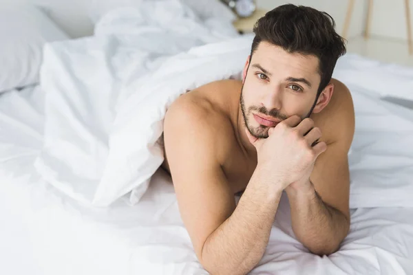 Bonito pensativo homem deitado na cama e olhando para a câmera — Fotografia de Stock