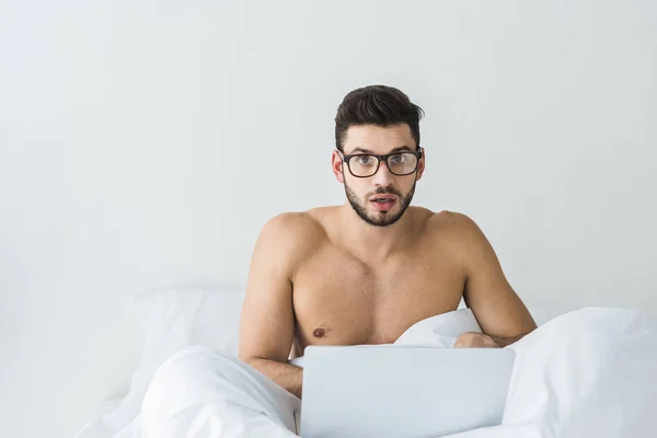 Shirtless bearded man in eyeglasses using laptop in bed — Stock Photo