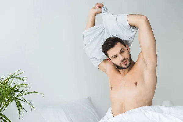 Schöner bärtiger Mann zieht sein T-Shirt im Schlafzimmer aus — Stockfoto