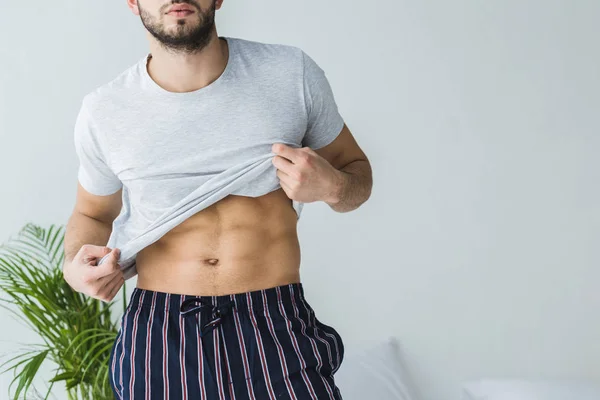 Cropped view of sexy man taking off his t-shirt in bedroom — Stock Photo