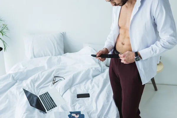 Businessman wearing belt near bed with digital devices — Stock Photo