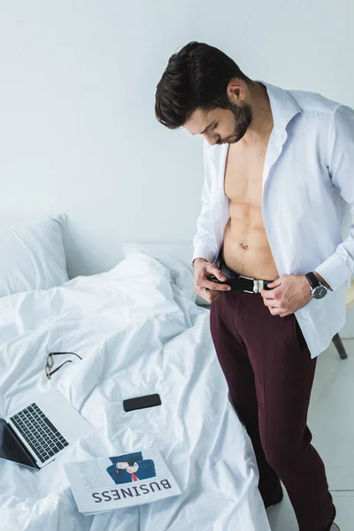 Uomo d'affari che indossa vestiti vicino al letto con dispositivi digitali e giornali — Foto stock