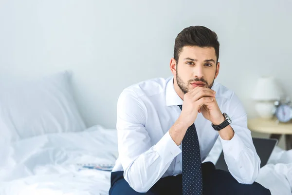 Guapo hombre de negocios en camisa blanca y corbata sentado en la cama - foto de stock