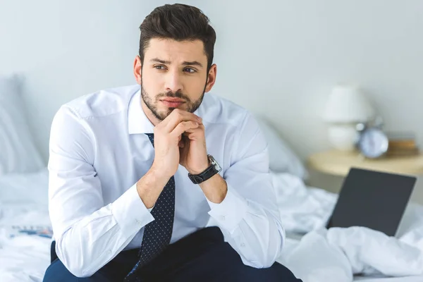 Handsome thoughtful businessman in white shirt and tie sitting on bed — Stock Photo