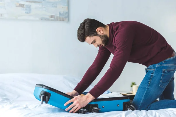 Handsome man packing baggage on bed for trip — Stock Photo