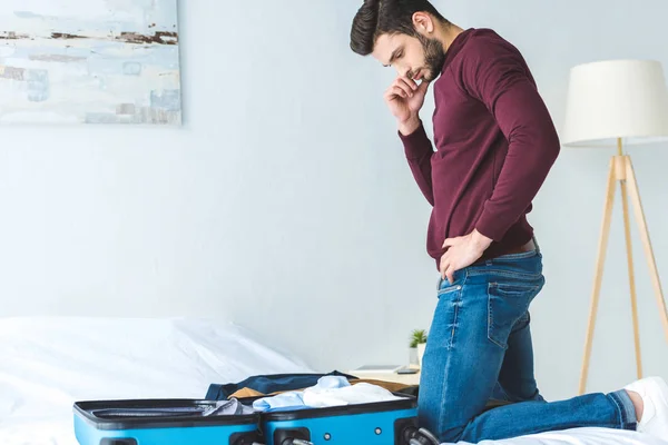 Thoughtful young man packing luggage on bed for travel — Stock Photo