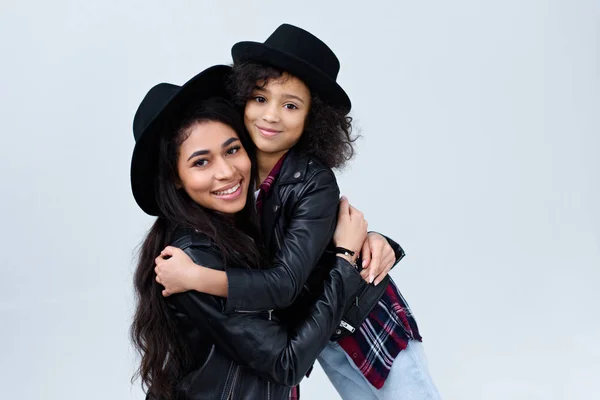 Lächelnd umarmen sich stilvolle Mutter und Tochter in ähnlichen Kleidern und blicken vereinzelt in die Kamera auf grau — Stockfoto
