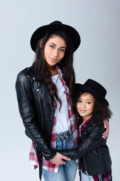 Mutter und Tochter in ähnlichen Kleidern umarmen sich und blicken vereinzelt in die Kamera auf grau — Stockfoto