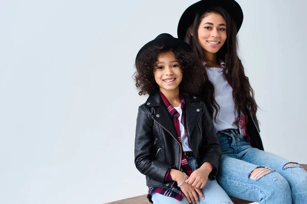 Mutter und Tochter in Hüten und Lederjacken sitzen vereint auf einer Bank in grau — Stockfoto