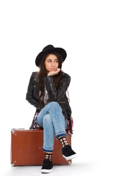 Élégante jeune femme en veste en cuir assise sur une valise vintage isolée sur blanc — Photo de stock