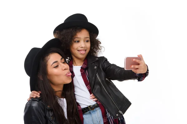 Elegante madre e hija tomando selfie con teléfono inteligente y muecas aisladas en blanco - foto de stock