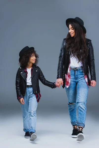 Happy fashionable mother and daughter walking together and holding hands on grey — Stock Photo