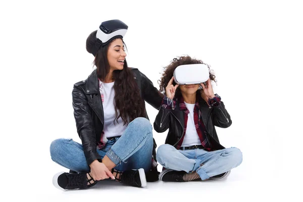 Happy mother and daughter in virtual reality headsets sitting on floor isolated on white — Stock Photo