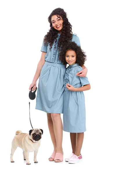 Young mother and daughter in similar dresses with pug on leash isolated on white — Stock Photo