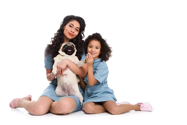 Щаслива молода мати і дочка сидять на підлозі з мопсом ізольовані на білому — стокове фото