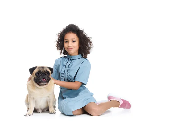 Glücklich kleines Kind im Kleid auf dem Boden sitzend mit Mops isoliert auf weiß — Stockfoto