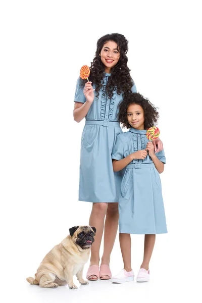 Madre e hija con caramelos de piruleta y pug aislados en blanco - foto de stock