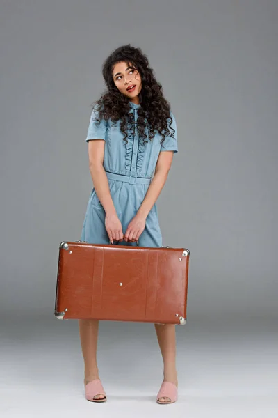 Jeune femme réfléchie avec valise vintage sur gris — Photo de stock