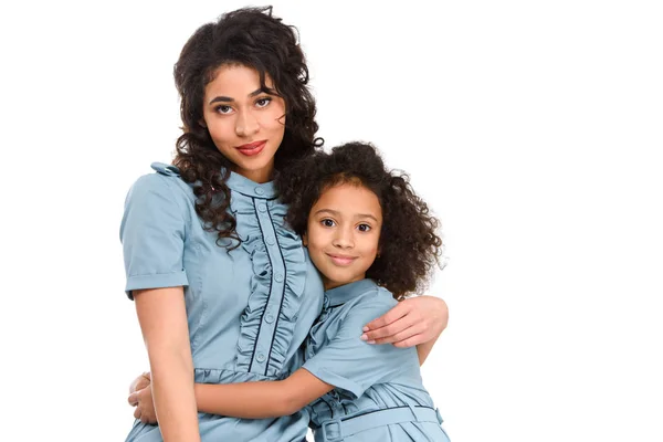 Madre e hija en vestidos similares abrazando y mirando a la cámara aislada en blanco - foto de stock