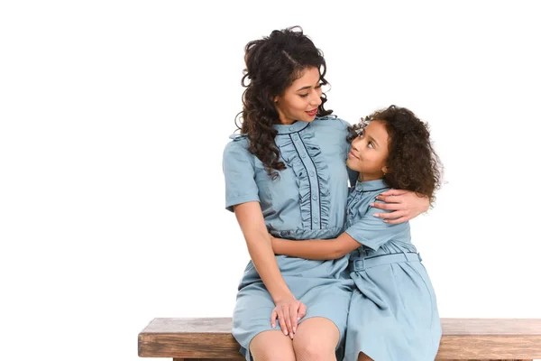 Mother and daughter embracing while sitting on bench isolated on white — Stock Photo