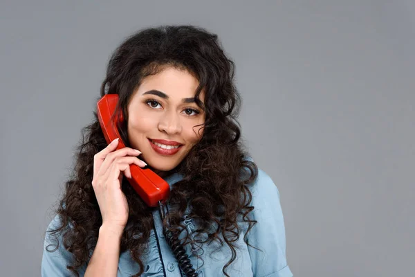 Glückliche junge Frau, die mit einem alten roten Telefon auf grau isoliert spricht — Stockfoto