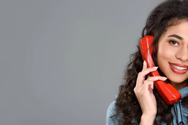 Lächelnde junge Frau, die mit einem alten roten Telefon spricht, isoliert auf grau — Stockfoto