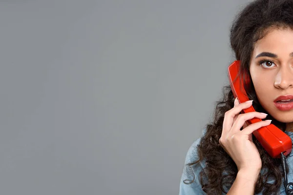 Schnappschuss einer jungen Frau, die mit einem roten Telefon spricht, isoliert auf grau — Stockfoto