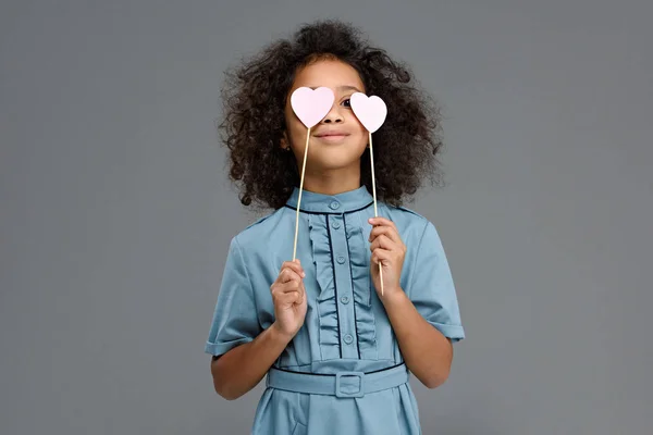Criança feliz cobrindo olhos com corações sinais isolados em cinza — Fotografia de Stock