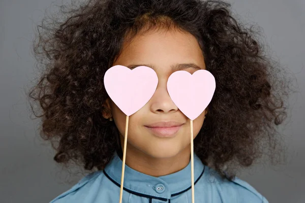 Nahaufnahme Porträt eines kleinen Kindes, das Augen mit Herzzeichen bedeckt, isoliert auf grau — Stockfoto