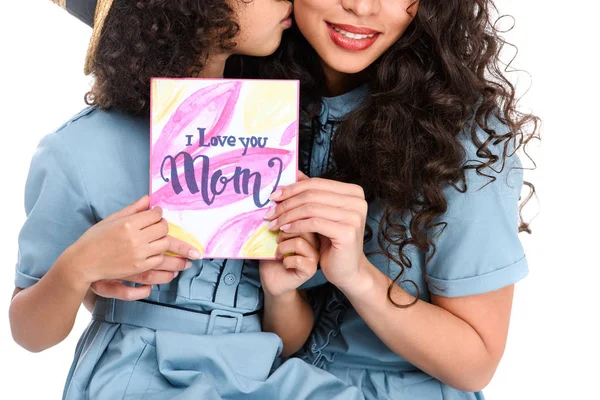 Plan recadré de fille avec la carte de vœux de la fête des mères embrassant sa mère isolée sur blanc — Photo de stock