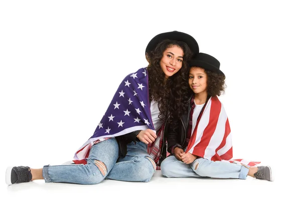 Mother and daughter covered in usa flag sitting on floor isolated on white — Stock Photo