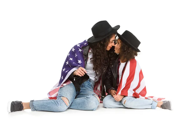 Beautiful mother and daughter covered in usa flag sitting on floor isolated on white — Stock Photo