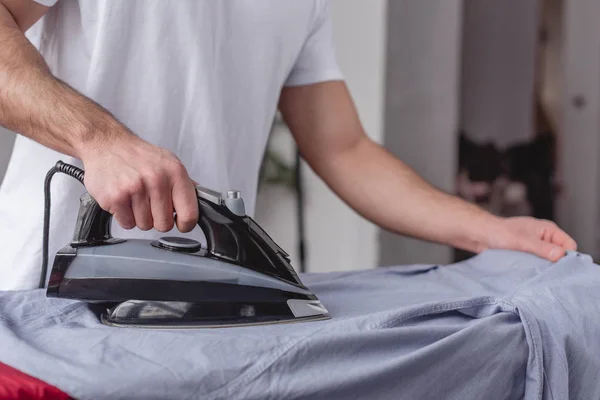 Abgeschnittenes Bild eines Mannes, der Hemd auf Bügelbrett im Wohnzimmer bügelt — Stockfoto